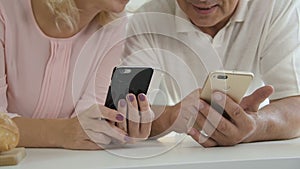 Elderly male holding phone and senior woman using smartphone at home.