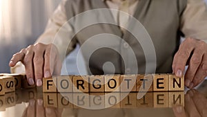 Elderly male making word forgotten of wooden cubes on table, dementia disorder