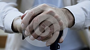 Elderly male putting hands on walking stick, retirement and disability, closeup