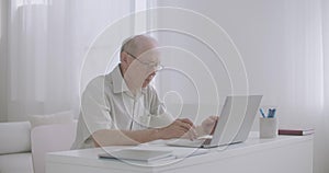 Elderly male specialist is working from home, typing and sending email by internet, using laptop