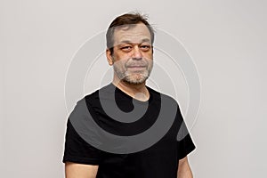 An elderly man 50-55 years old with a beard on a white background, wearing a black T-shirt, looks confidently