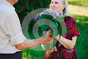 An elderly man of 80 years old gives flowers to his wife