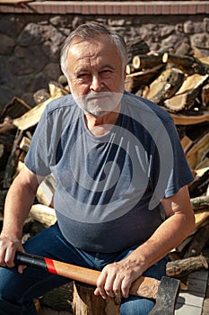 Elderly man with ax sits in front of pile of firewood