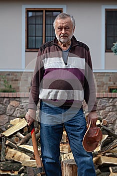 Elderly man with ax stands in front of pile of firewood