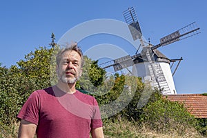 An elderly man with a beard against a background of a windmill and a summer rural landscape.