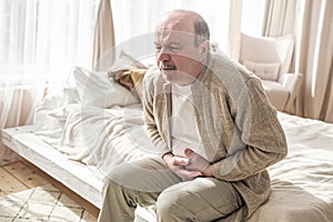 Elderly man with bellyache holding stomach with his hand