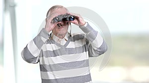 Elderly man with binoculars, blurred background.
