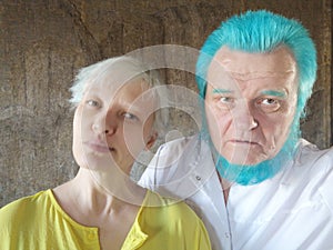 elderly man with blue beard and girl gray hair are standing next to each other, posing for camera and filming themselves on phone