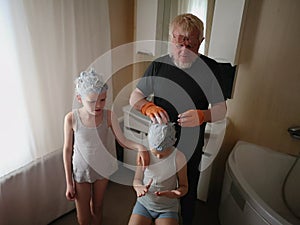 elderly man with blue beard and orange gloves smears child& x27;s head with blue dye to bleach hair. The family is happy together