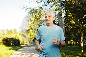 An elderly man in a blue T-shirt is jogging through a summer park.