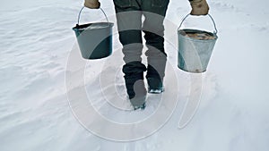 An elderly man with buckets in winter carries water from a well. Handheld shooting.