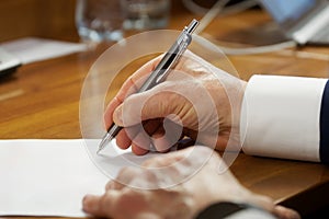 An elderly man in a business suit with cuffs, writing with a fountain pen on a piece of paper. Concept of writing a will or