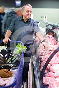 Elderly man chooses beef in supermarket