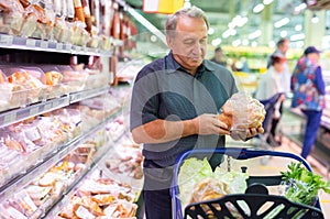 Elderly man chooses chicken meat in supermarket