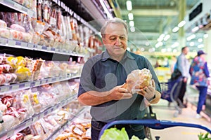 Elderly man chooses chicken meat in supermarket