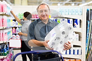 Elderly man chooses toilet paper in supermarket