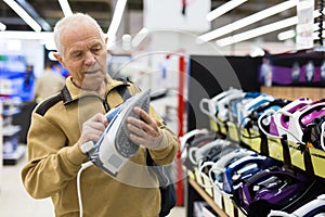 Elderly man choosing iron in showroom of electrical appliance store