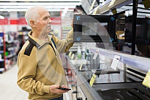 elderly man choosing microwave oven in showroom of electrical appliance store