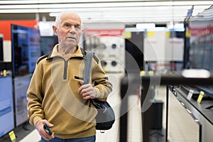 elderly man choosing TV in showroom of electronics store