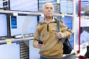 elderly man choosing TV in showroom of electronics store