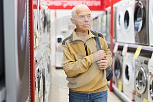 Elderly man choosing washing machine in showroom of electrical appliance store