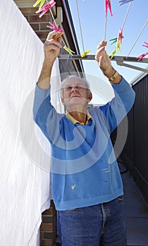 Elderly Man Collecting Pegs From Clothesline.