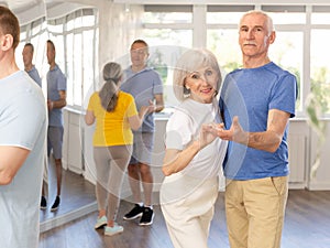 Elderly man in dance hall with female partner and dances Latin rumba. Hobby, healthy lifestyle concept