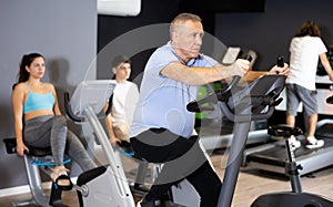 Elderly man doing cardio training on stationary bike in gym