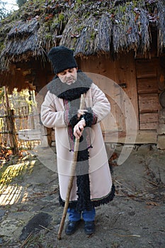 An elderly man in a doodle hat and sheepskin coat looks at his watch