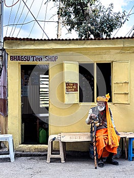 An elderly man dressed in bright orange in front of a tea shop in Mcleodganj