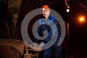 An elderly man dressed in work overalls and a helmet stands near the old inverted vogonetki. Miner