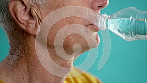 An elderly man drinks water from a bottle isolated on a blue background. Health and hydration concept
