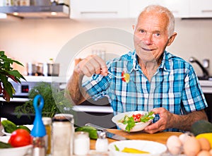 Elderly man eating fresh vegetable salad at home