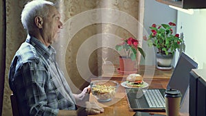 An elderly man emotionally rooting for his favorite team watching a sports game on a laptop at home
