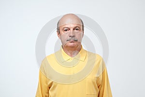 Elderly man emotions, portrait of serious senior caucasian man looking at camera against gray wall