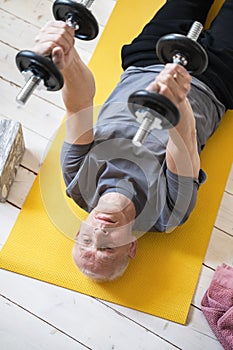 Elderly man exercising with a dumbbells during his workout in home gym