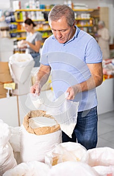 Elderly man filling polybag with wheat flour in grocery store