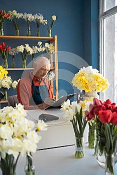 An elderly man florist sits at the table and writes intently on paper.