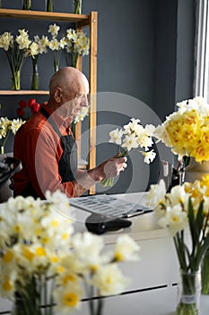 An elderly man florist is sitting making bouquet.