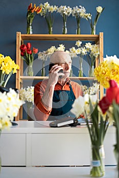 An elderly man flower seller takes an order for flower delivery over the phone.
