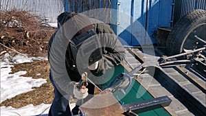 An elderly man foreman repairs a car trailer using electric arc welding.