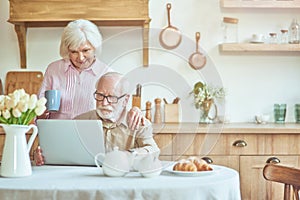 Elderly man in glasses busy while working on computer at home