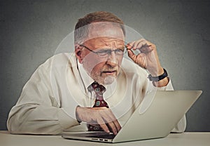 Elderly man with glasses confused with laptop software
