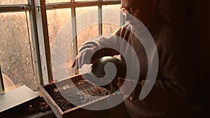 Elderly man glasses picks up military helmet brushing dust off in house window