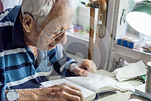 Elderly man with glasses reading writings in notebook near the window at home