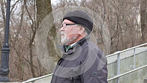 an elderly man with a gray-haired beard and wearing a hat puts on glasses.