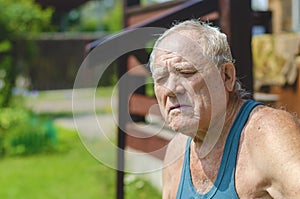 An elderly man in a green T-shirt is basking in the sun with his eyes closed