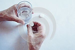 Elderly man hands taking medicine pill with a glass of water