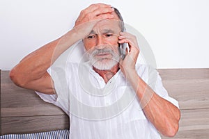 Elderly man with headache in bed calling the doctor