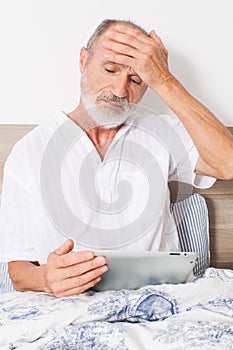 Elderly man with headache in bed looking for a doctor